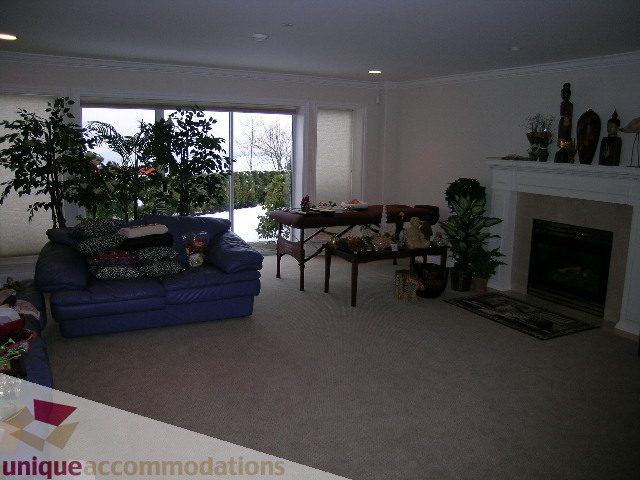 Spacious living room with large windows, plush blue couch, fireplace, and indoor plants. - 1659 Langton Place, West Vancouver