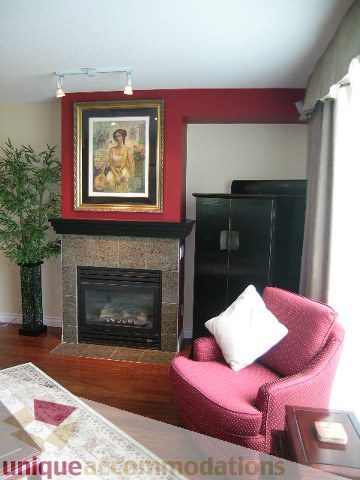 Living room with red accent wall, fireplace, and pink armchair. - 305 - 1030 Quebec Street, Vancouver Downtown