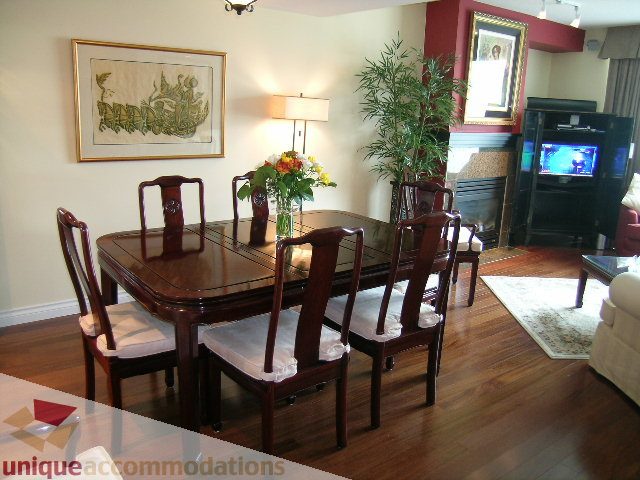 Furnished dining area with wooden table, chairs, and a vase of flowers, hardwood floors, and a TV. - 305 - 1030 Quebec Street, Vancouver Downtown