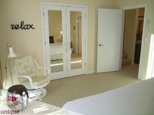 Spacious bedroom with mirrored closet doors, cozy seating, and "relax" sign. - 305 - 1030 Quebec Street, Vancouver Downtown