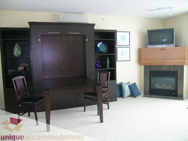 Living room with built-in entertainment center, fireplace, and dining area with chairs. - 305 - 1030 Quebec Street, Vancouver Downtown