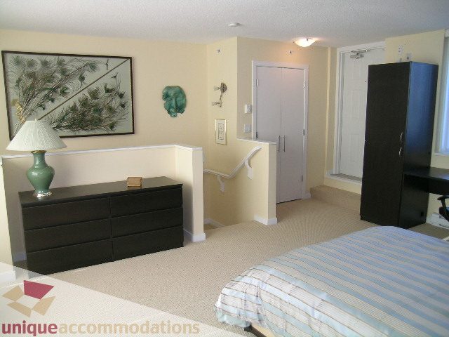 Spacious bedroom with striped bedding, dark dresser, and wall art. - 305 - 1030 Quebec Street, Vancouver Downtown