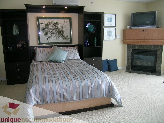 Furnished bedroom with striped bedding, built-in shelves, and a fireplace. - 305 - 1030 Quebec Street, Vancouver Downtown