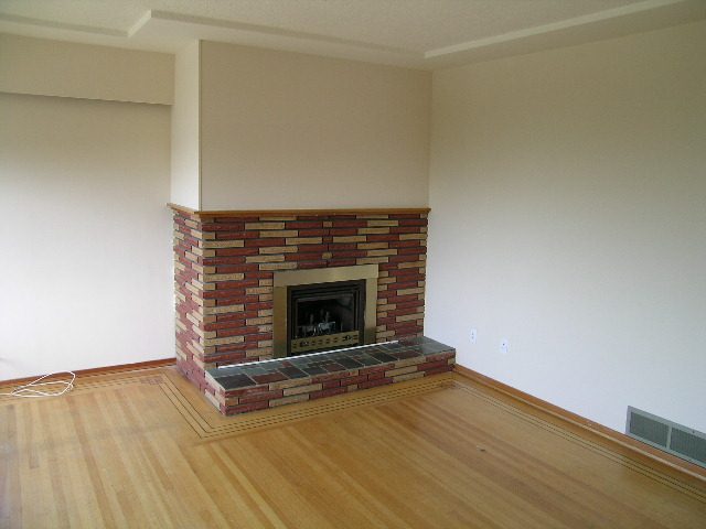 Spacious living room with hardwood floors, brick fireplace, and open layout. - 660 Blueridge Ave, North Vancouver