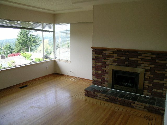 Spacious living room with hardwood floors, brick fireplace, and city view. - 660 Blueridge Ave, North Vancouver
