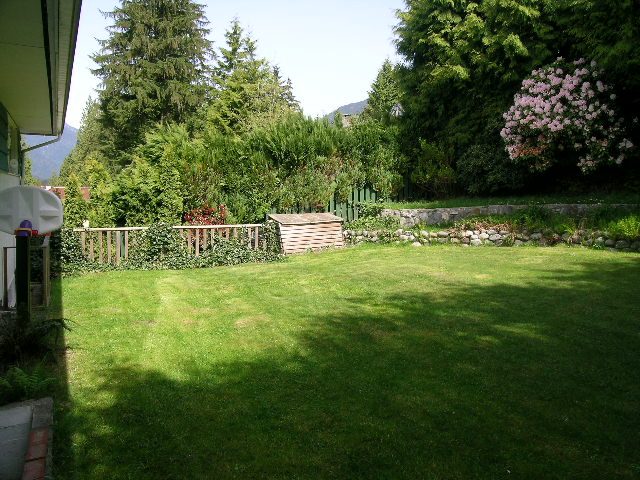 Spacious backyard with lush green lawn, stone garden, and blooming flowers. - 660 Blueridge Ave, North Vancouver