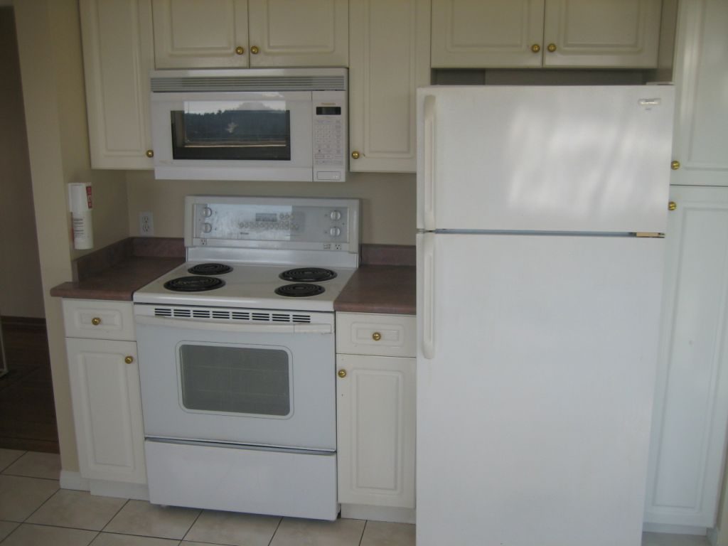 Bright kitchen with white appliances, granite countertops, and a city view through the microwave. - 660 Blueridge Ave, North Vancouver