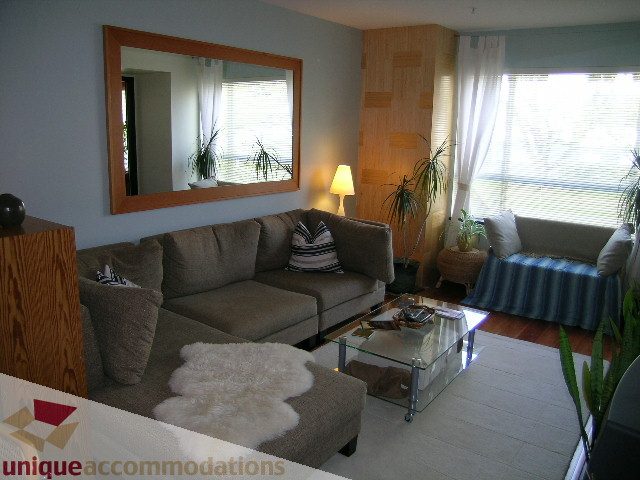 Furnished living room with large mirror, wooden accent wall, and glass coffee table. - 201-365 E 1st Ave, North Vancouver