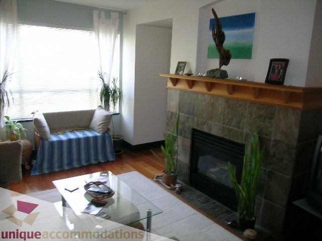 Furnished living room with hardwood floors, glass coffee table, and stone fireplace. - 201-365 E 1st Ave, North Vancouver