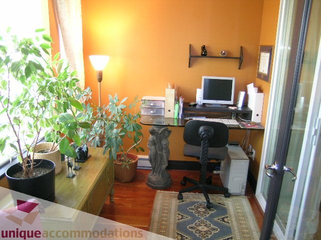 Furnished 1-bedroom + den with hardwood floors, desk, and potted plants. - 201-365 E 1st Ave, North Vancouver