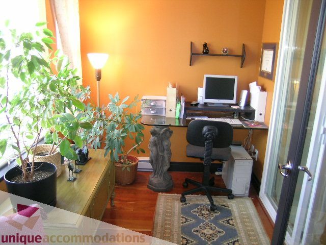 Furnished 1-bedroom + den with hardwood floors, desk, and potted plant. - 201-365 E 1st Ave, North Vancouver
