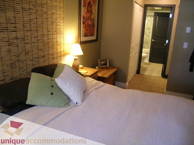 Furnished 1-bedroom + den with cozy bedding, bamboo wall, and open bathroom access. - 201-365 E 1st Ave, North Vancouver