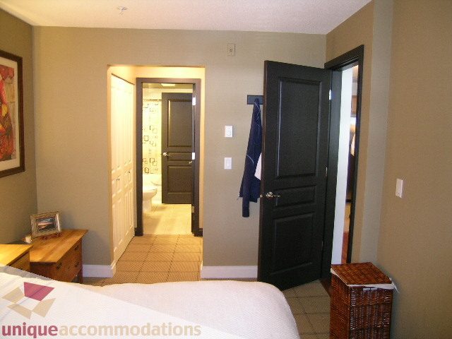 Furnished bedroom with open door leading to bathroom, light wood furniture, and neutral decor. - 201-365 E 1st Ave, North Vancouver