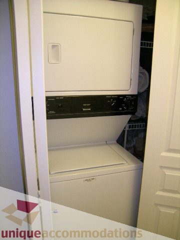 Bright laundry room with stacked washer and dryer, white cabinets. - 201-365 E 1st Ave, North Vancouver