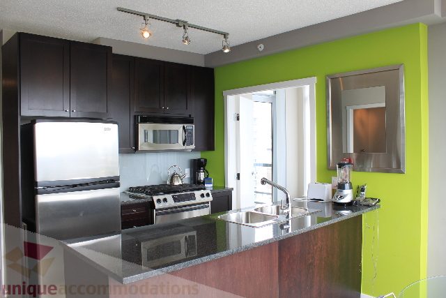 Bright kitchen with modern appliances, stainless steel counters, and green accent wall. - 2103 - 1001 Homer Street, Vancouver Downtown