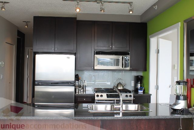 Bright kitchen with dark cabinets, stainless steel appliances, and a green accent wall. - 2103 - 1001 Homer Street, Vancouver Downtown