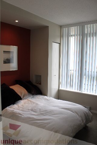 Furnished bedroom with red accent wall and large window with blinds. - 2103 - 1001 Homer Street, Vancouver Downtown