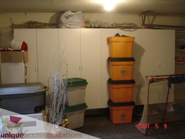 Storage area with stacked orange bins and white cabinets, cluttered with various items. - 100 Lions Bay Avenue, West Vancouver