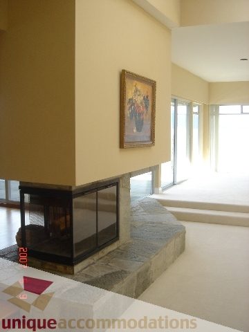 Bright living room with stone fireplace and large windows, leading to a bright outdoor area. - 100 Lions Bay Avenue, West Vancouver
