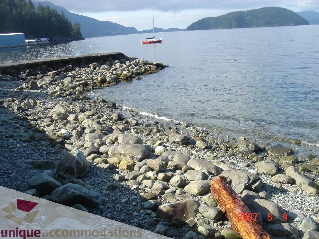 Beachfront house with pebbled shoreline and distant sailboat. - 100 Lions Bay Avenue, West Vancouver