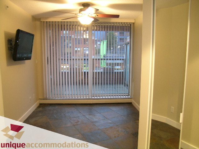 Bright living room with sliding glass door leading to a balcony, featuring a flat-screen TV mounted on the wall and a...