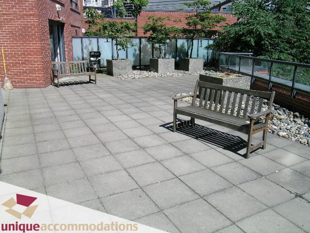 Furnished patio with wooden benches and pebble garden, brick wall backdrop. - 2C - 199 Drake Street, Vancouver Downtown