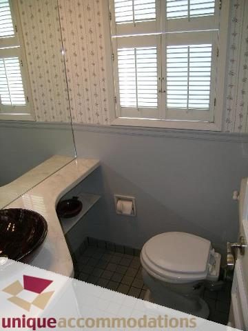 Furnished bathroom with white toilet and sink, patterned wallpaper, and window with shutters. - 4177 West 15th Avenue, Vancouver West Side