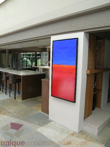 Bright living room with modern decor, large flat-screen TV, red artwork, and open kitchen in the background. - 455 Keith Road, West Vancouver
