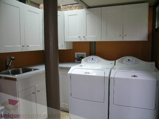 Bright laundry room with white cabinets and stainless steel sink, modern appliances. - 455 Keith Road, West Vancouver