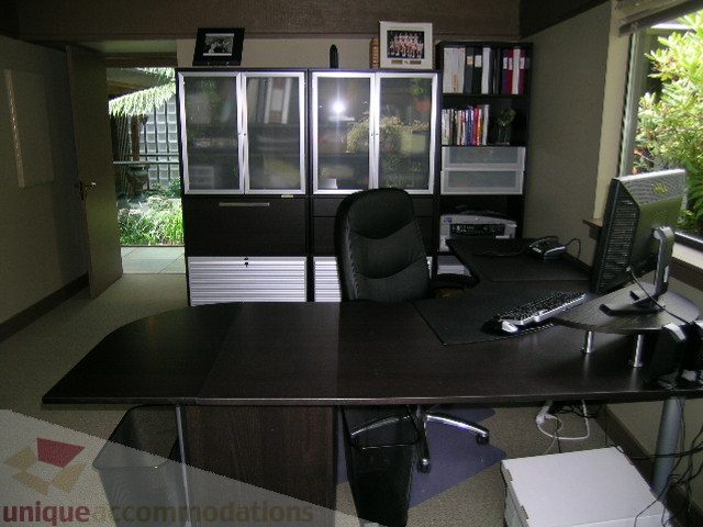 Furnished office with dark wood desk, black office chair, and bookshelves. - 455 Keith Road, West Vancouver