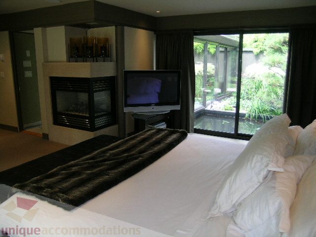 Furnished bedroom with cozy fireplace, large window view, and plush bedding. - 455 Keith Road, West Vancouver