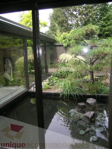 Furnished living room with large windows, greenery, and a tranquil pond view. - 455 Keith Road, West Vancouver
