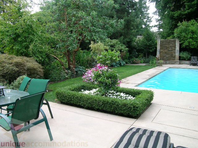 Furnished patio with green chairs, table, and a stunning pool surrounded by lush greenery. - 455 Keith Road, West Vancouver