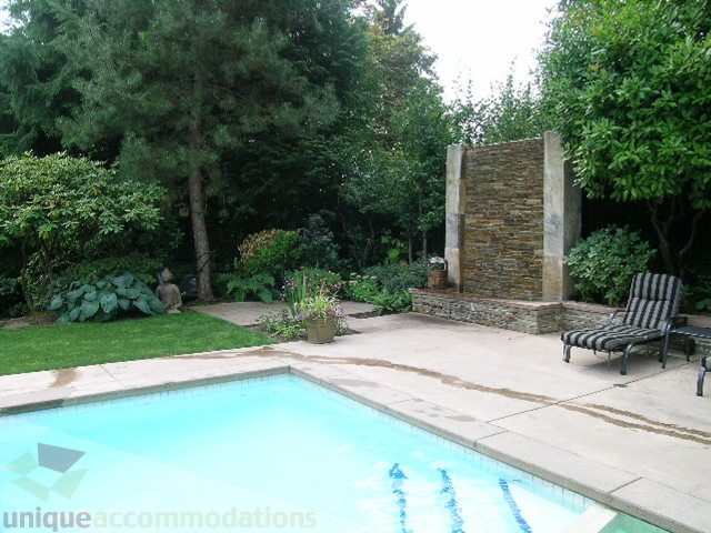 Spacious backyard with pool, stone wall, and lush greenery. - 455 Keith Road, West Vancouver