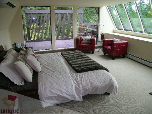 Bright sunlit bedroom with large windows, red armchairs, and cozy bedding. - 455 Keith Road, West Vancouver