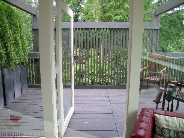 Furnished living room with a red leather couch and wooden deck access. - 455 Keith Road, West Vancouver