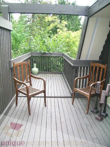 Furnished balcony with wooden chairs and greenery, leading to a house with 4 bedrooms and a den. - 455 Keith Road, West Vancouver
