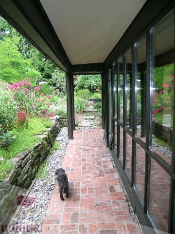 Bright sunroom with brick floor, garden view, and black dog. - 455 Keith Road, West Vancouver