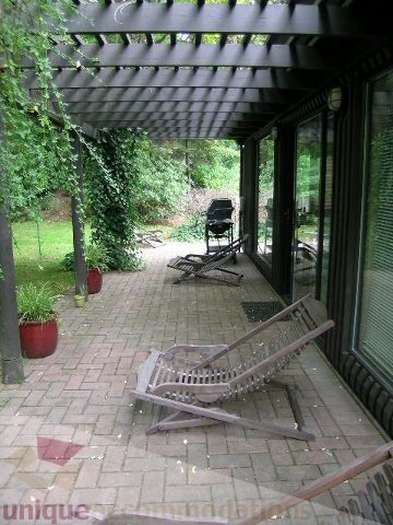 Furnished patio with wooden furniture and a pergola, surrounded by greenery. - 455 Keith Road, West Vancouver
