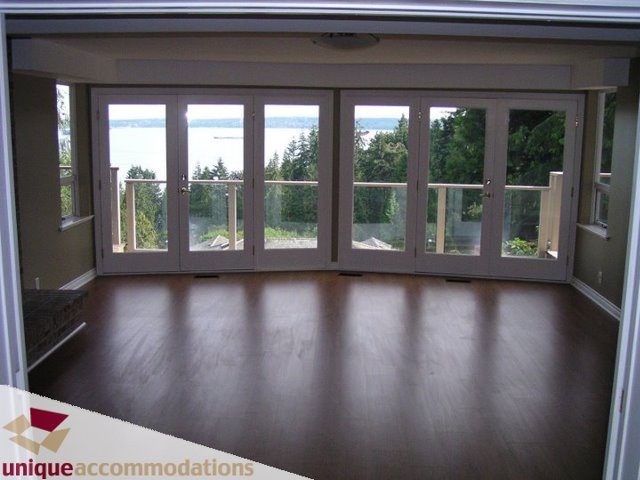 Bright living room with hardwood floors and a stunning view of the forest and water beyond. - 3580 Westmount Court, West Vancouver
