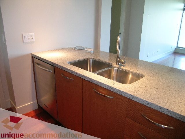 Bright kitchen with granite countertops and stainless steel sink, hardwood floors visible in background. - 1302 - 3355 Cypress Pl, West Vancouver