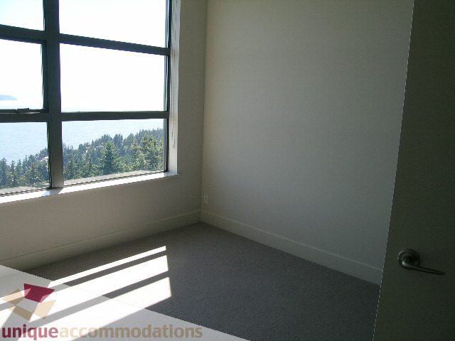 Bright living room with large window offering a scenic view, light gray carpet, and white walls. - 1302 - 3355 Cypress Pl, West Vancouver