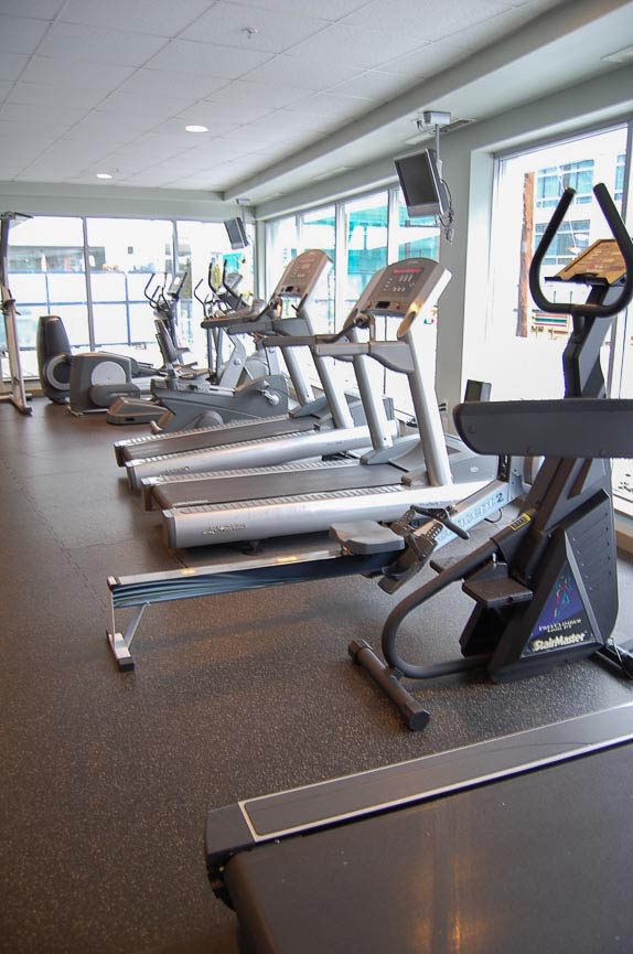 Modern gym with sleek treadmills and large windows showcasing downtown Vancouver skyline. - 3209 - 928 Beatty Street, Vancouver Downtown
