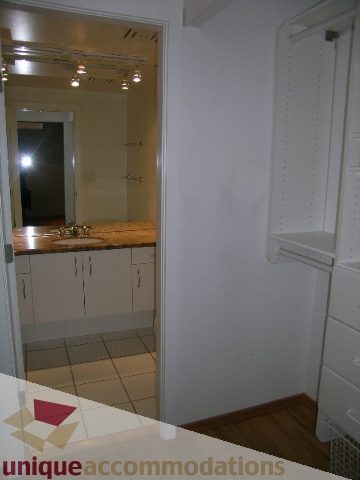 Bright kitchen with white cabinets and countertop, hardwood floors, and a view of the bathroom. - 402-1155 Mainland St, Vancouver Downtown