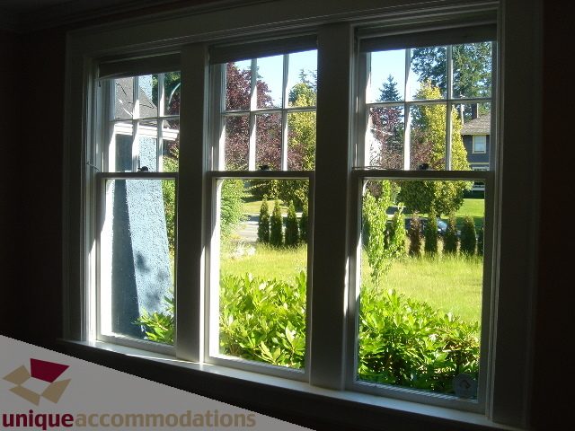 Bright living room with large windows showing greenery and a view of houses across the street. - 1475 W 33rd Ave, Vancouver West Side