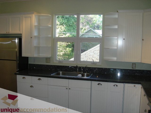 Bright kitchen with black countertops and white cabinets, featuring a window view of greenery. - 1475 W 33rd Ave, Vancouver West Side