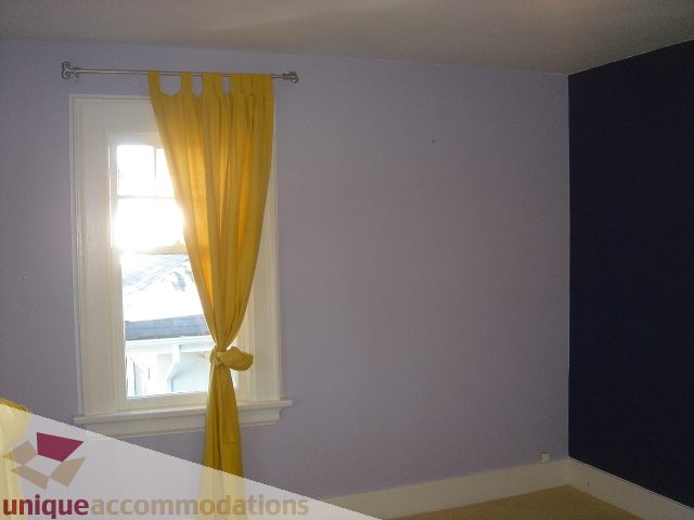 Bright bedroom with purple walls, yellow curtains, and a window view. - 1475 W 33rd Ave, Vancouver West Side