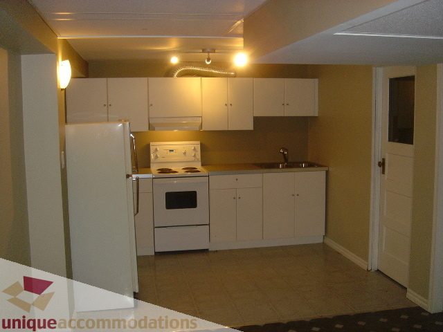 Bright kitchen with white cabinetry and stainless steel appliances, open to a living area with tiled flooring. - 1475 W 33rd Ave, Vancouver West Side