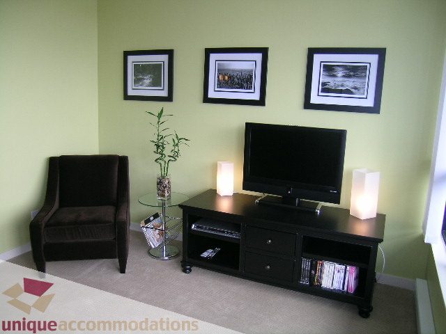 Bright living room with black entertainment center, framed artwork, and cozy armchair. - 2707 - 928 Homer Street, Vancouver Downtown