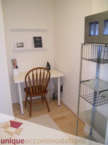 Compact dining area with wooden chairs and a small table, featuring a modern kitchenette in the background.